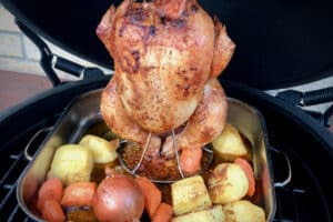 photo of vertical roast chicken with veg in a tray on the bbq