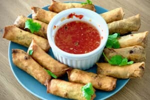 photo of lots of Thai Spring Rolls with a small bowl of dipping sauce in the centre of the plate