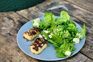 phot of grilled Halloumi and pea salad on a grey plate next to a bbq