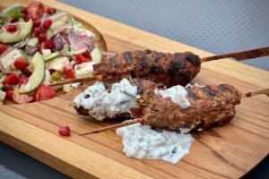 Photo of Lamb Kofta on wooden skewers on a board with yogurt dip