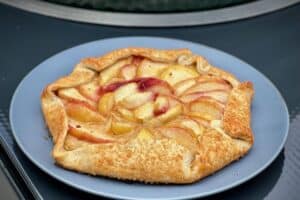 photo of a Flat peach galette on a grey plate next to a bbq
