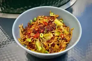 photo of a dish of Hot Dry Noodles next to a bbq