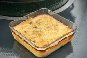 photo of cooked Cheesy Leek Gratin in a glass dish next to a bbq