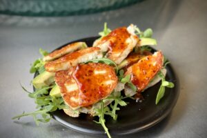 photo of a Chilli Halloumi Sandwich on a black plate next to a bbq