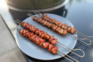a photo of Chicken Heart Skewers on a plate next to a bbq