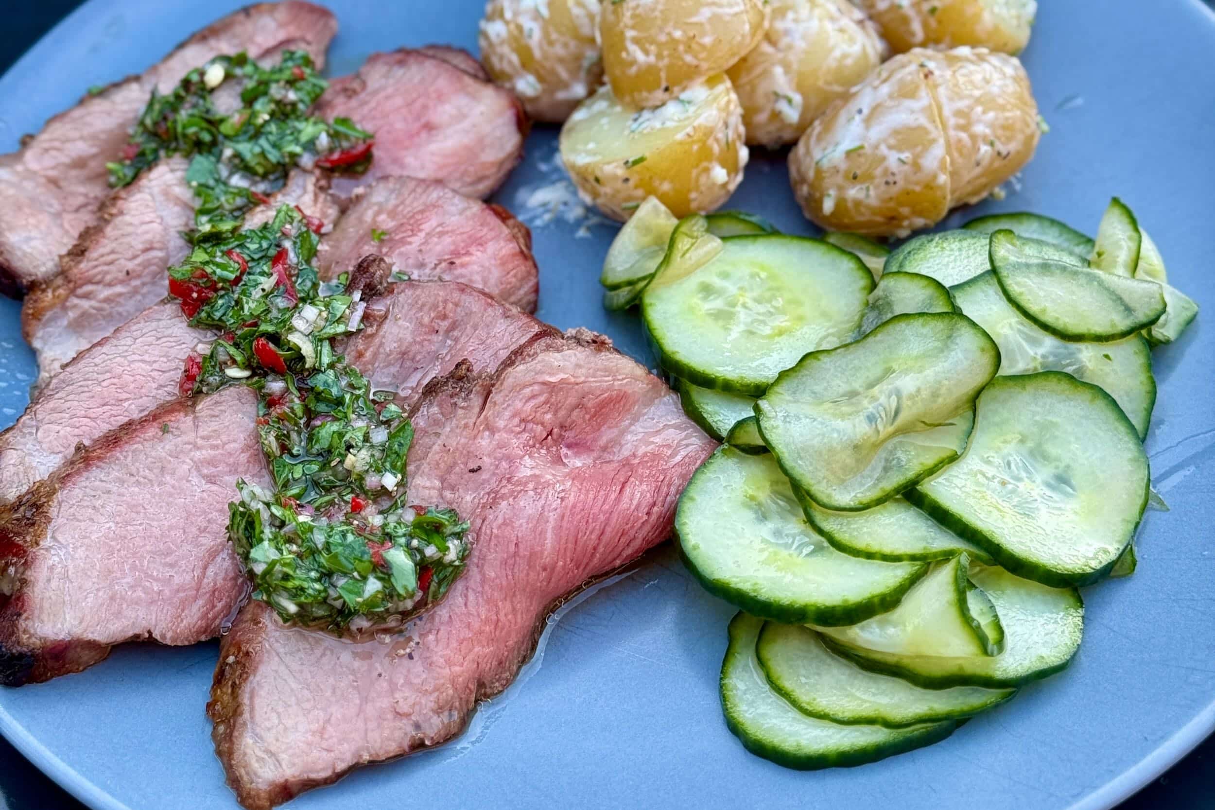 A photo of sliced Iberico Pressa, next to a potato salad and a cucumber salad